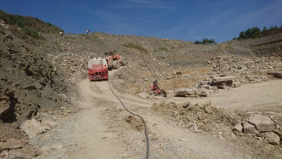 Tankwagen auf der Sohle eines Steinbruchs, der Schlauch liegt über den Schotter zum Radlader